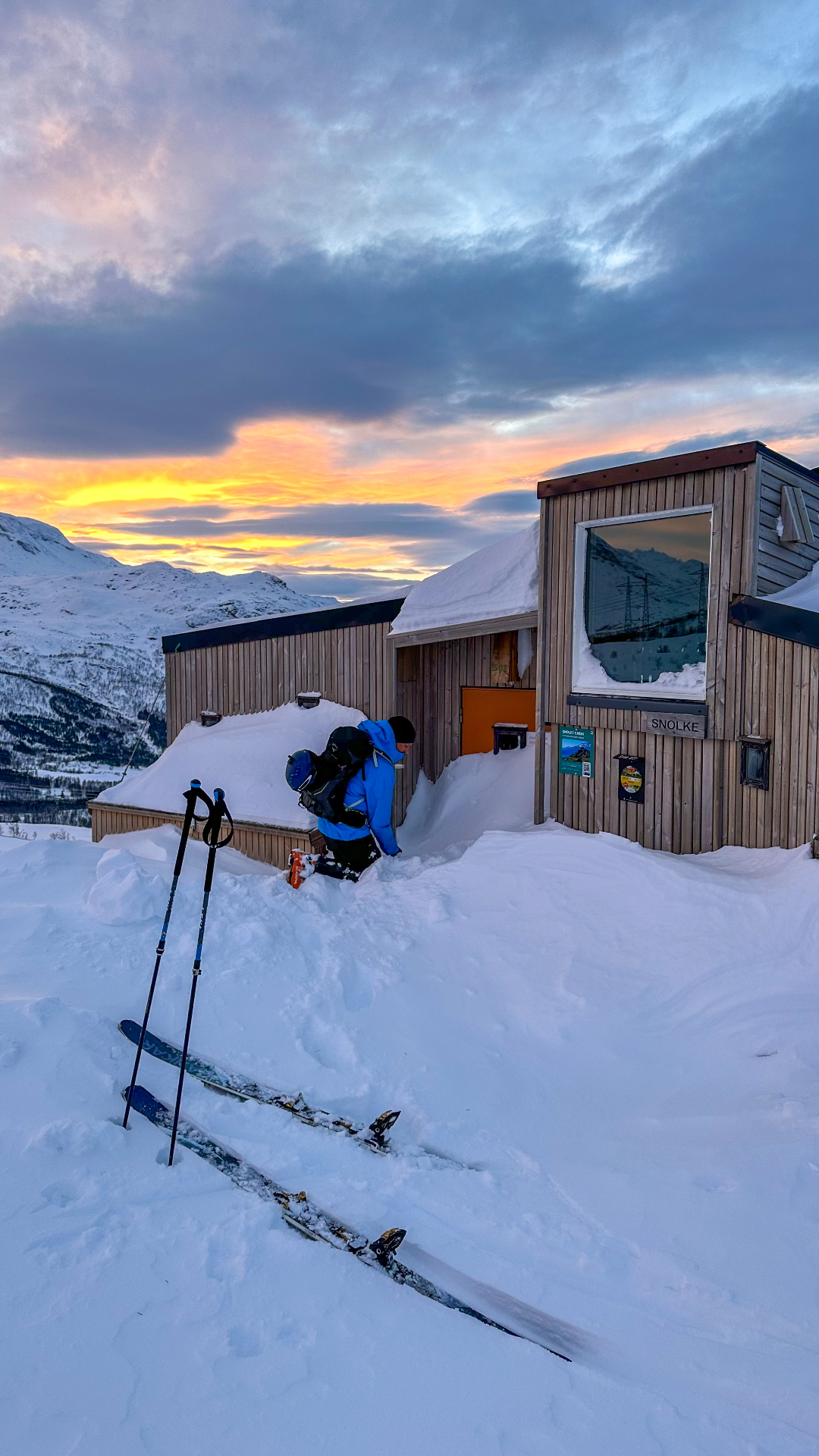 Ein Skifahrer mit Skiern vor der Hütte an einem Winterabend